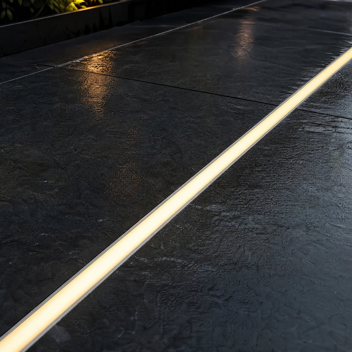 LED floor profile set flush into dark paving, lit warm white at dusk