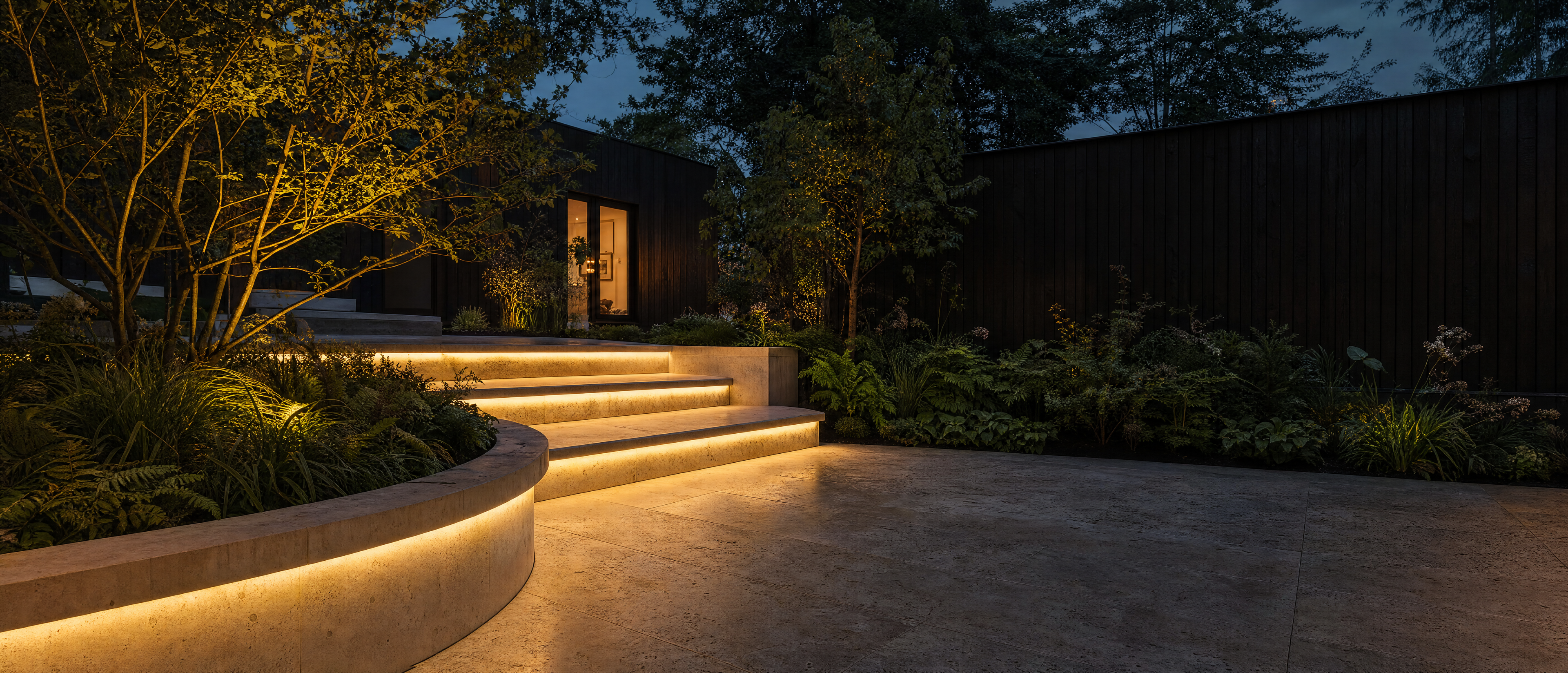 Warm white LED lighting beneath limestone steps and a curved planter in a landscaped courtyard at dusk
