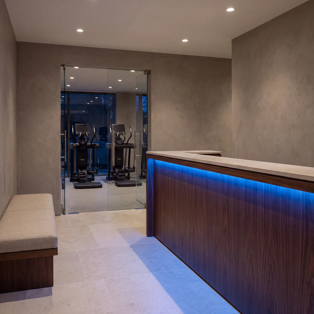 Blue SCOB LED strip lighting beneath a walnut gym reception counter, with seating and exercise equipment beyond; installation illustration.