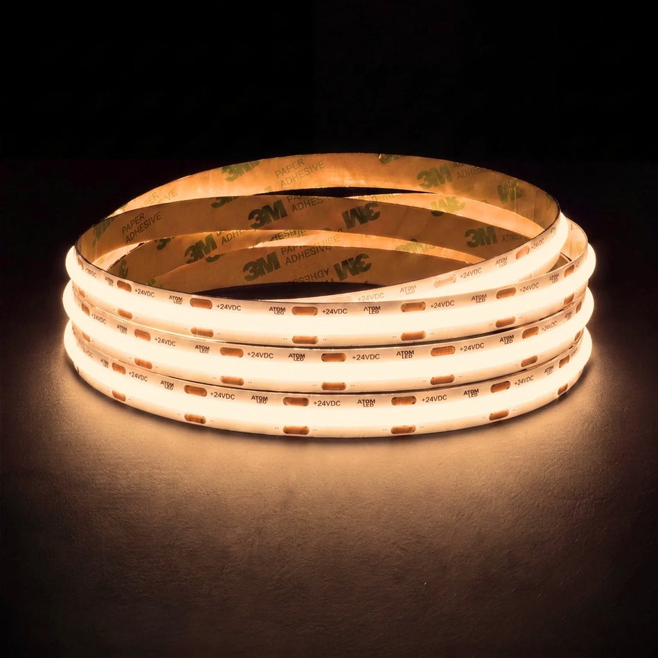 Warm white 3000K SCOB LED strip coil illuminated on a dark background, 24V DC and 10mm wide, with copper connection pads