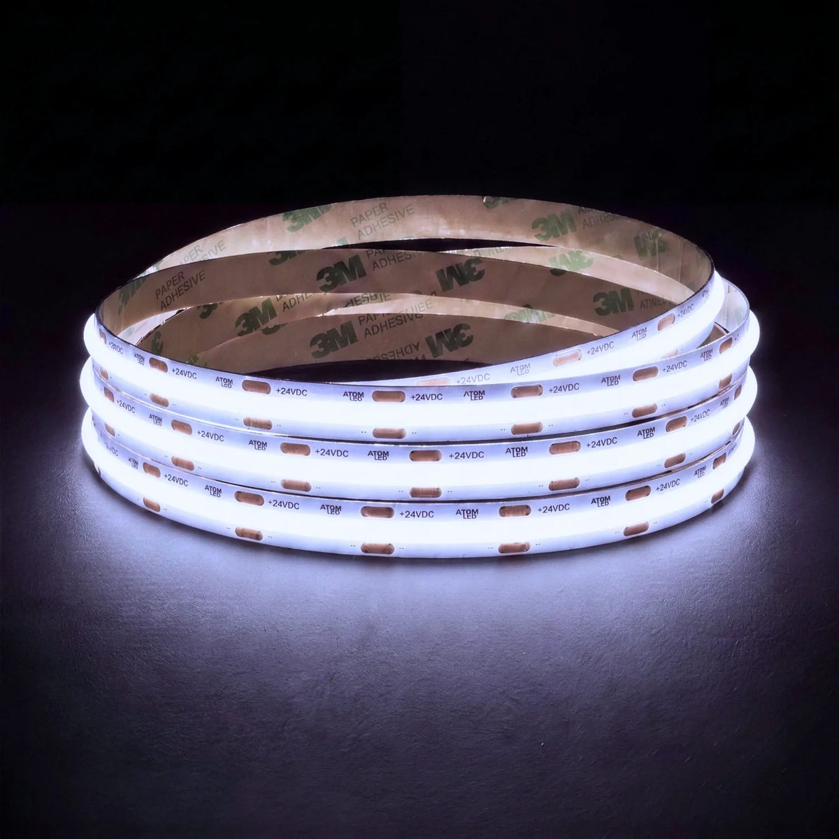 Cool white 6500K SCOB LED strip coil illuminated on a dark background, 24V DC and 10mm wide, with copper connection pads
