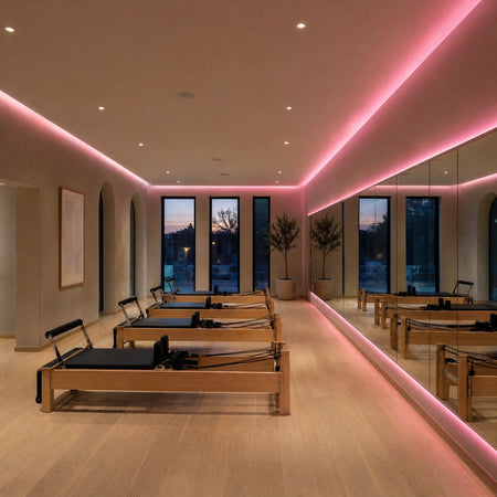 Illustrative Pilates studio with pink SCOB LED ceiling-cove lighting, a backlit mirror and timber reformer machines