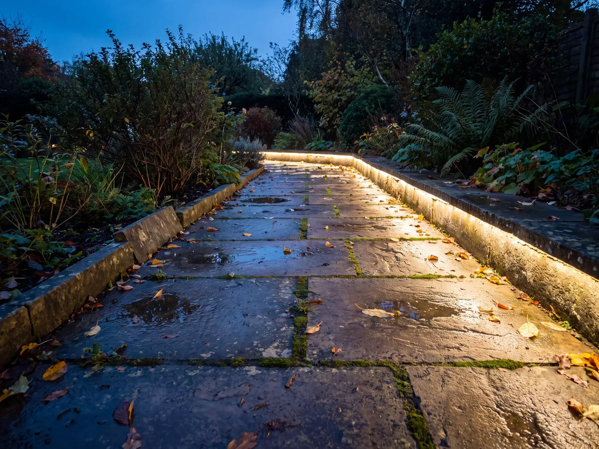 Warm white IP67 LED strip lighting running along a garden path edge at dusk in a British garden